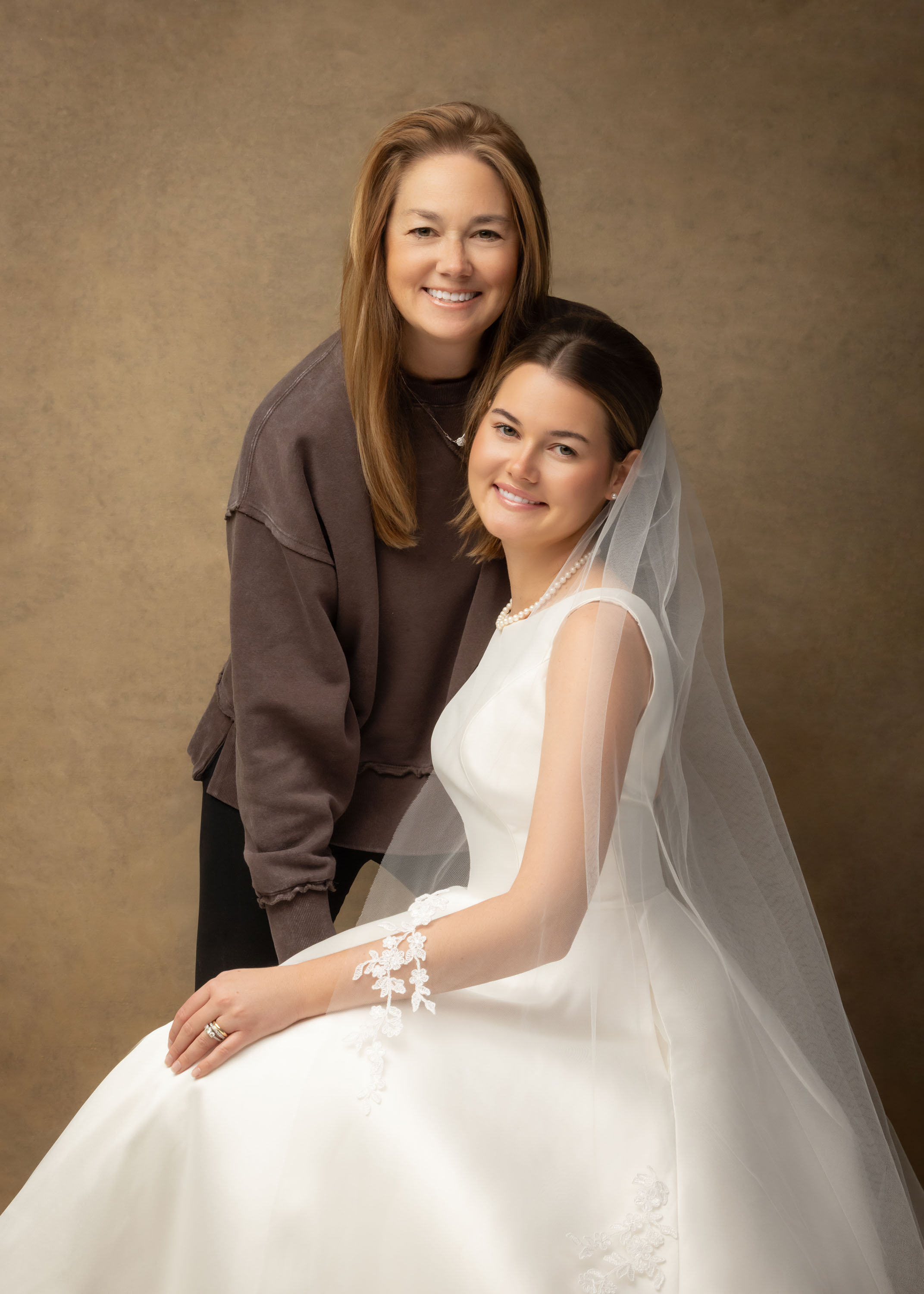 Mother and daughter together in a studio portrait, the daughter wearing her wedding dress